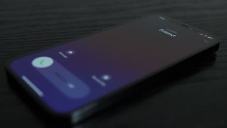 Close-up-shot-of-an-iPhone-receiving-a-call-from-a-friend-on-black-wooden-table