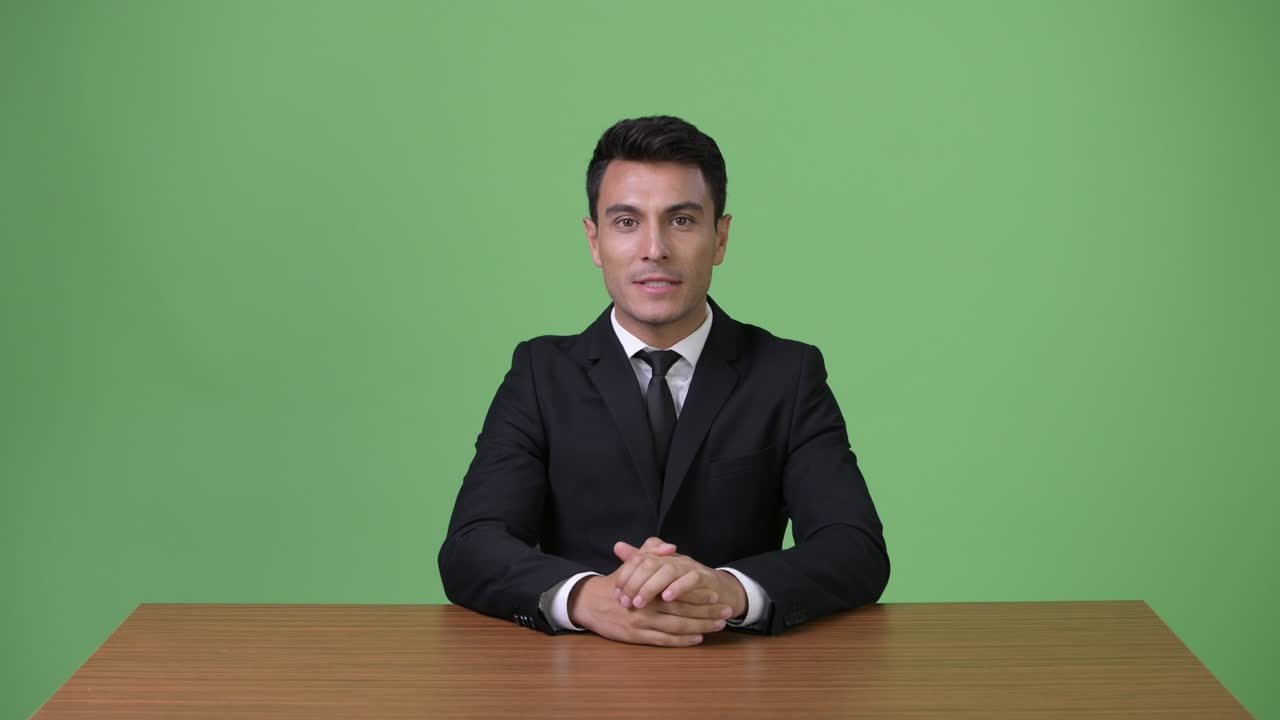 Young handsome Hispanic businessman against green background
