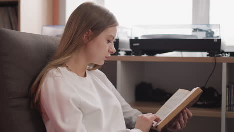 woman reads book sitting in armchair. concentrated student studies information with literature in public reading hall. blonde lady with novel