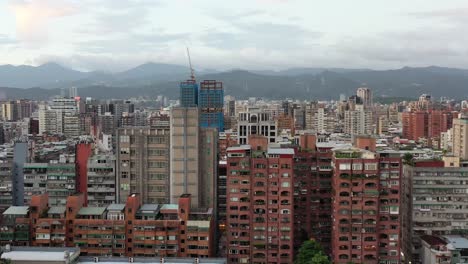 aerial tracking shot capturing overly crowded high density population living in taipei city, rows of old ageing high rise apartments facade in downtown xinyi district, with mountainous background