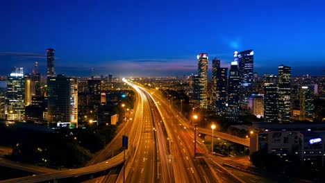 aerial view of a city skyline and busy highway transitioning from sunset to night, with vibrant lights illuminating tall buildings and roads