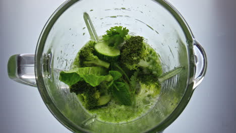 Blender start mixing vegetable fruits herbs close up top view. Vitamin food.