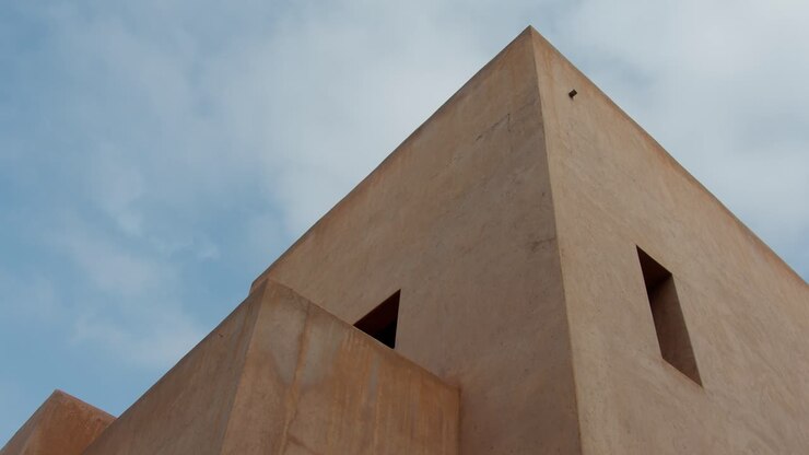 Tomada estática em ângulo baixo focando nas formas geométricas nítidas e na fachada detalhada de um edifício em Marrakech, Marrocos, sob luz solar intensa