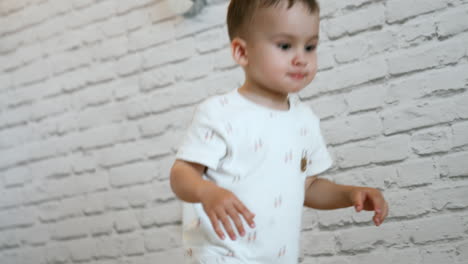 cute caucasian toddler stands holding by the white wall. baby boy moves quickly forward to get something from the table.