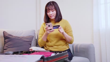 young woman making hotel reservation with credit card while preparing suitcase with clothes