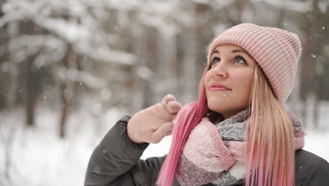 Slow-motion,-winter-woman-in-the-woods-watching-the-snow-fall-and-smiling-looking-at-the-sky-and-directly-into-the-camera.