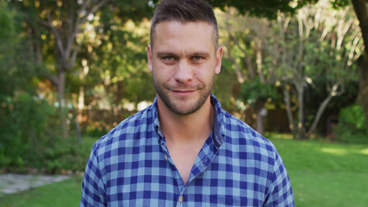 retrato de un hombre caucásico feliz de pie en el jardín sonriendo a la cámara