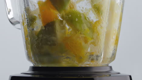 dropping pieces fruits blender with spinning blades close up. vitamin nutrition