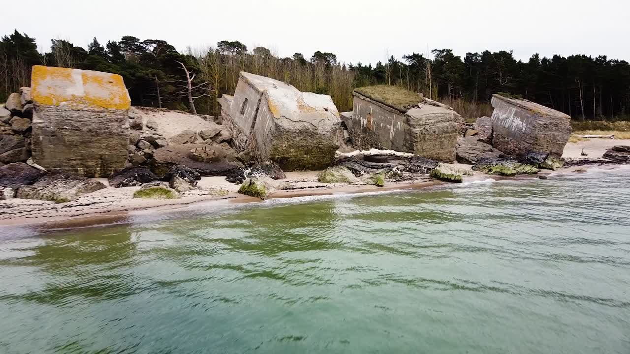 Dronefoto af en forladt befæstningsbygning ved kysten ved Karosta Nordlige Forter på stranden ved Østersøen i Liepaja på en overskyet forårsdag, stille hav, bredt etablerende droneoptagelse der bevæger sig bagud