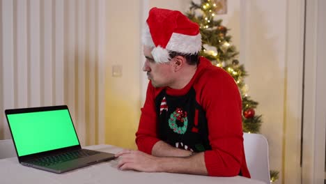 Hombre-Festivo-Con-Sombrero-De-Santa-Y-Suéter-Mirando-La-Pantalla-Verde-De-La-Computadora-Portátil-Con-Expresiones-De-Pensamiento-Preguntándose-Qué-Hacer