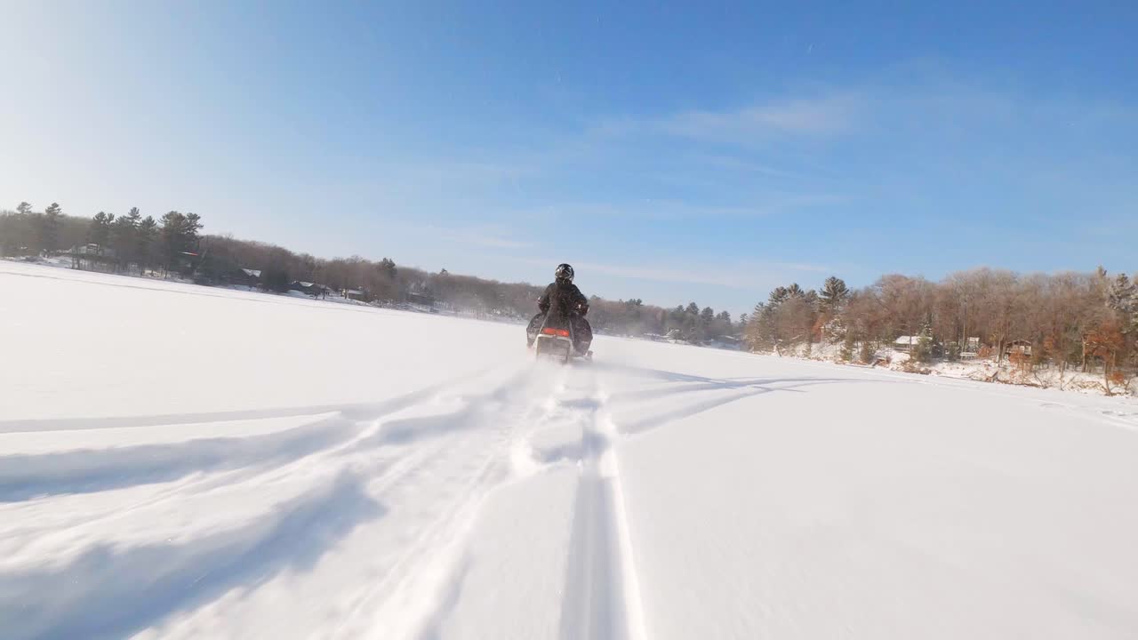 FPV drone following person driving snowmobile on a frozen lake covered with thick snow during the day