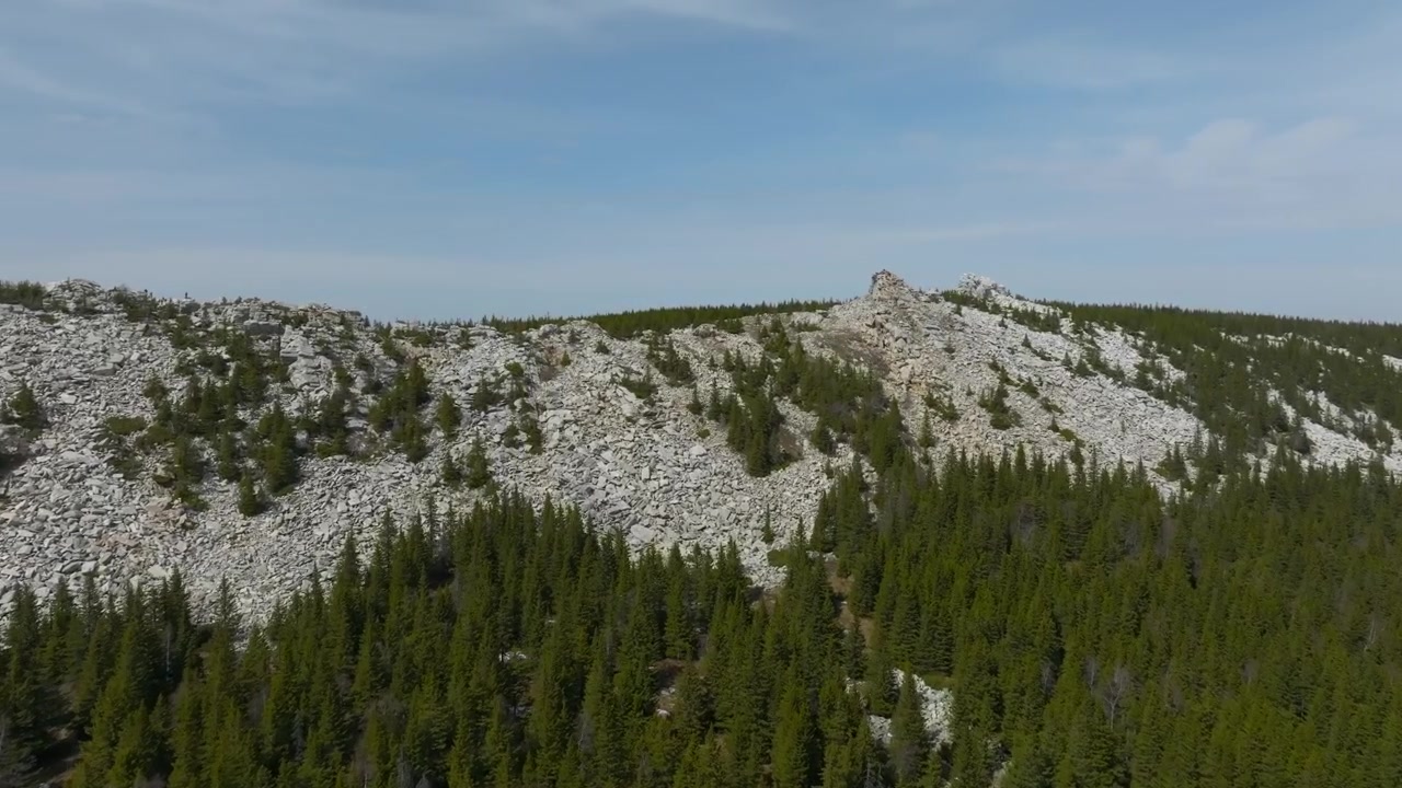 Droneoptagelser af en stenet bjergryg over tæt stedsegrøn taigaskov under blå himmel i Zyuratkul Nationalpark, Tjeljabinsk oblast, Rusland