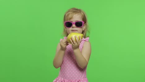 child in pink swimsuit and sunglasses eats a green pear. chroma key