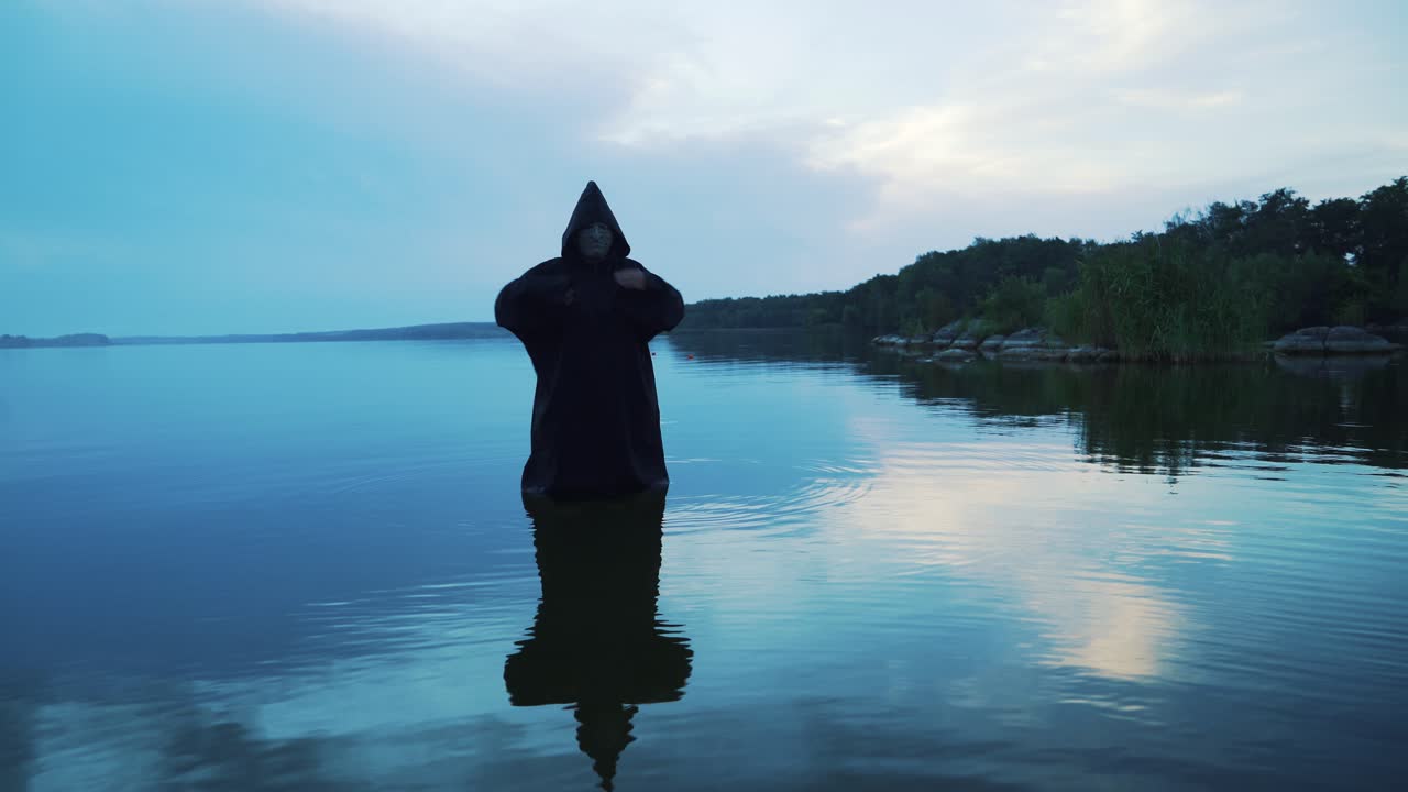 Scary figure in black mantle in the river. Halloween costume.