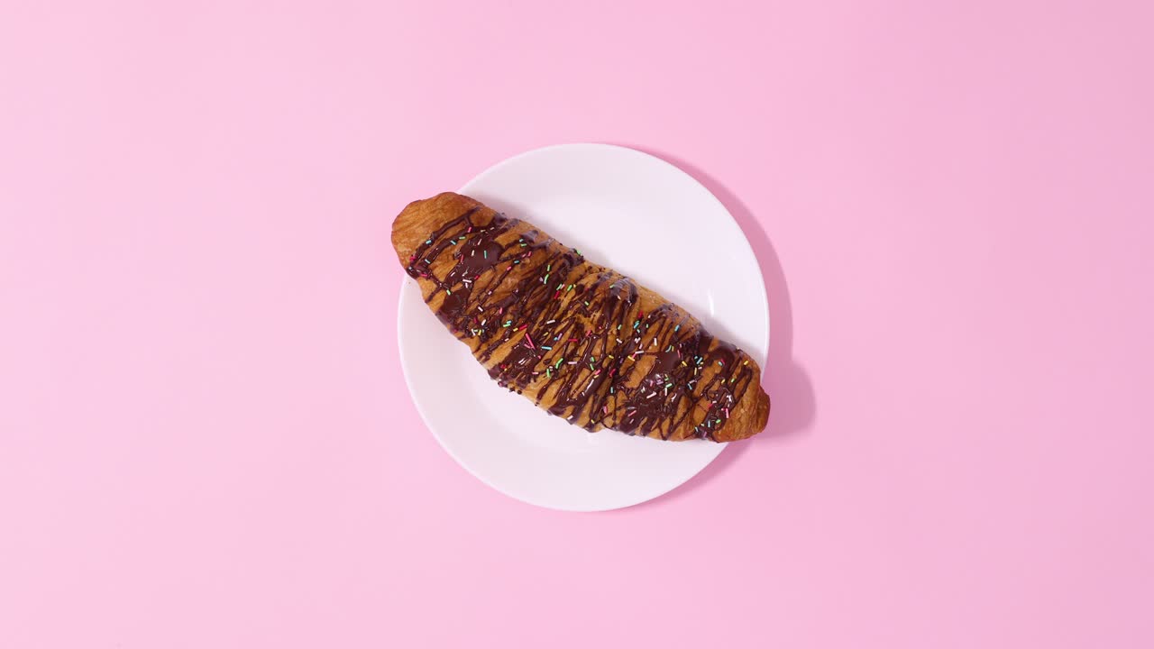croissant de chocolate fresco girando en una placa blanca sobre un fondo rosa pastel. detenga el movimiento
