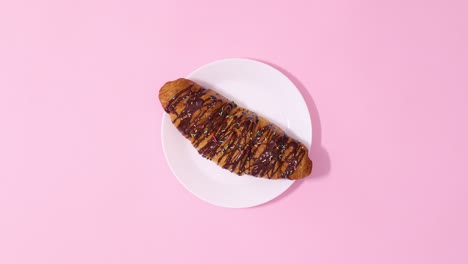 fresh chocolate croissant rotating on white plate on pastel pink background. stop motion