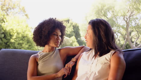 smiling mother and adult daughter sitting on couch outdoors, enjoying conversation and bonding