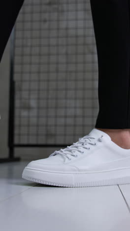stylish snow-white sport shoes with laces on a model. man wearing black trousers and modern sneakers posing in studio. close up. vertical video