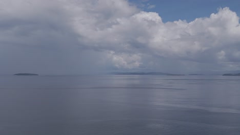 large moody grey storm clouds over a calm seascape with small islands in the far distance