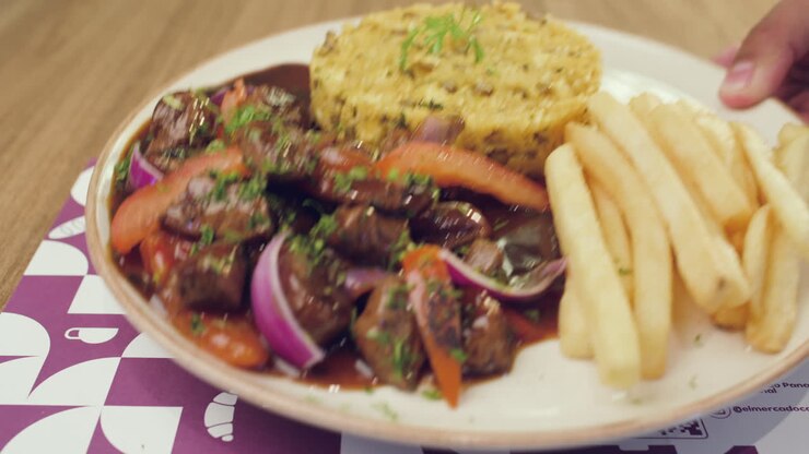 Primer plano de un camarero colocando un plato de ternera salteada con arroz y patatas fritas; comida caliente y bien presentada en un restaurante.