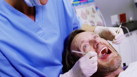 Dentist-examining-a-male-patient-with-dental-tools-