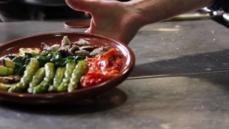 mano del chef mostrando la ensalada vegana que acaba de preparar, con espárragos, champiñones, espinacas, calabacín y pimiento rojo asado