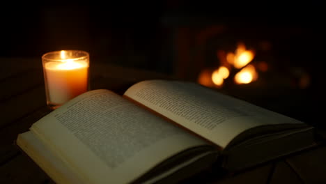 an old vintage antique book open on a table lit by candlelight with an open fire and fireplace in a dark room