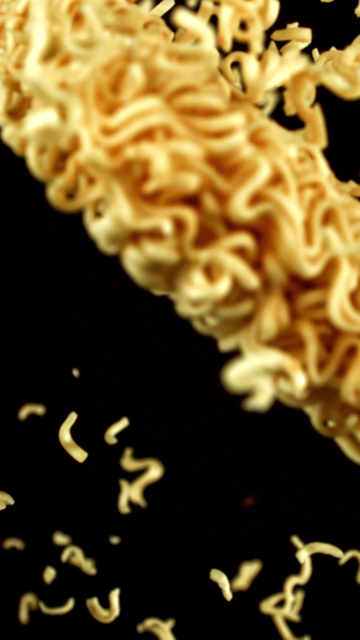 Noodles istantanei secchi che cadono al rallentatore su sfondo nero