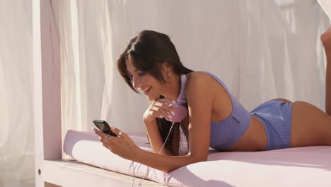 Brunette-girl-lying-on-beach-bed-and-using-phone.
