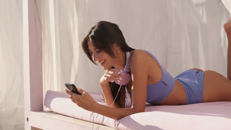 brunette girl lying on beach bed and using phone.