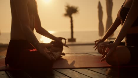 Close-up-shot-of-a-girl-in-a-black-sports-summer-uniform-and-a-guy-in-black-shorts-meditating-on-a-Red-Mat-on-a-sunny-beach