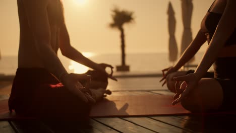 close-up shot of a girl in a black sports summer uniform and a guy in black shorts meditating on a red mat on a sunny beach