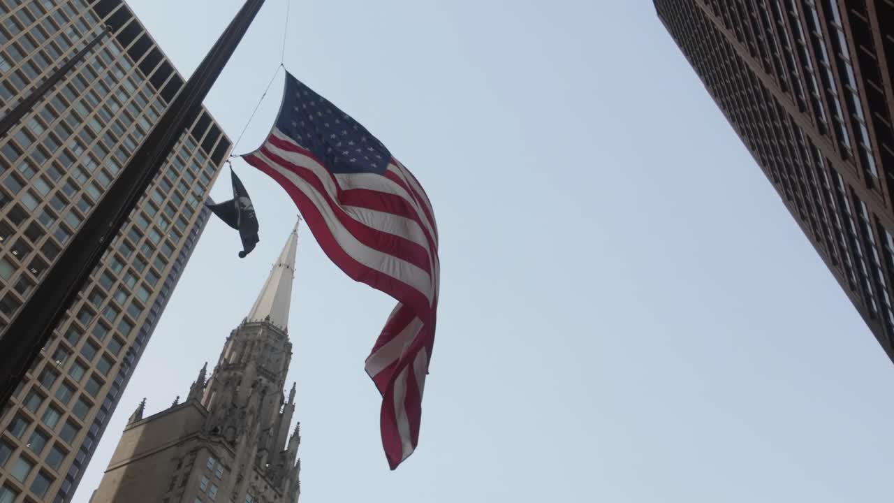 Una gigantesca bandiera americana circondata da alti edifici nel centro di Chicago mentre un uccello vola via