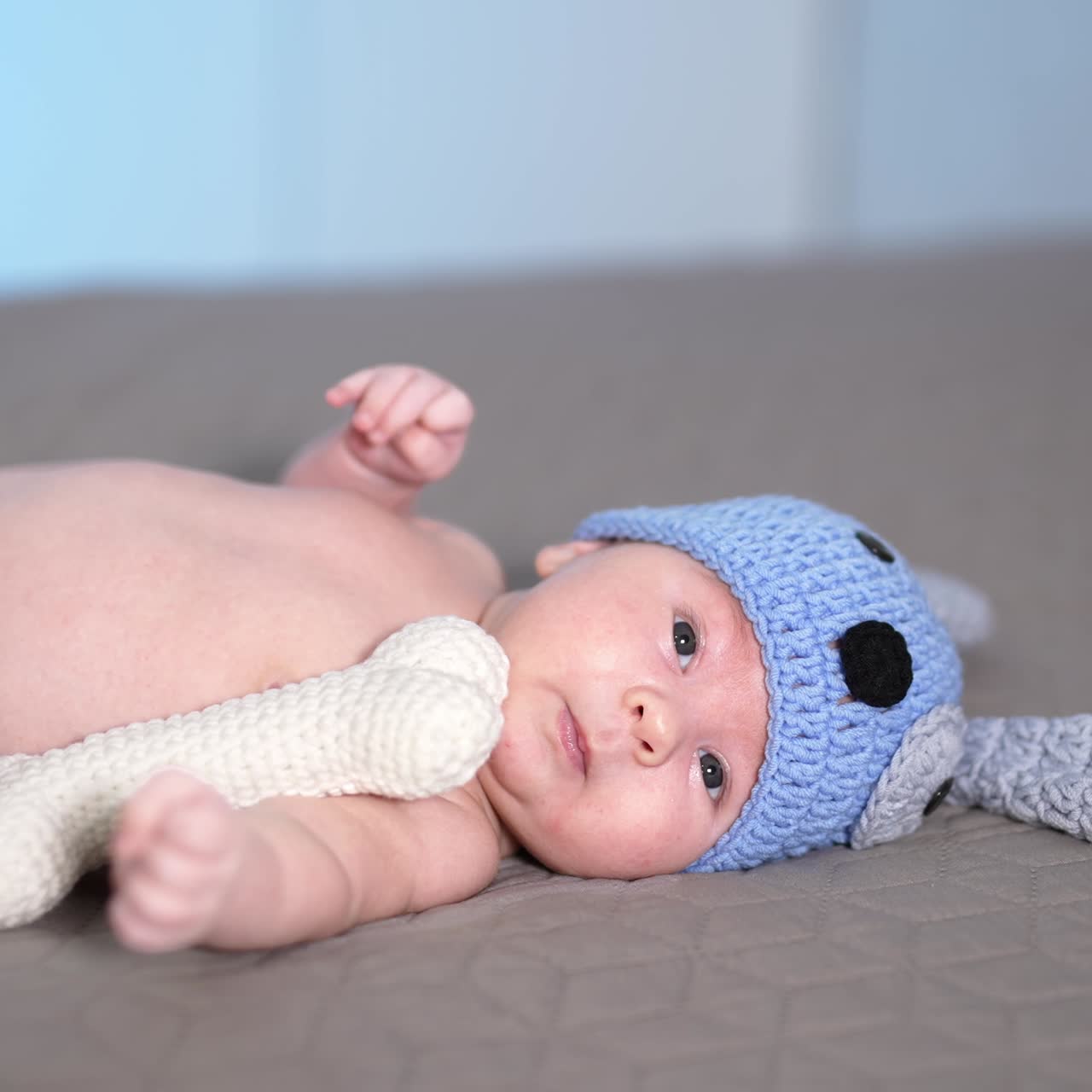 Adorable baby lying on the big bed. Baby in a nice costume of a puppy lies and moves his little feet. Little kid in a funny knitted costume