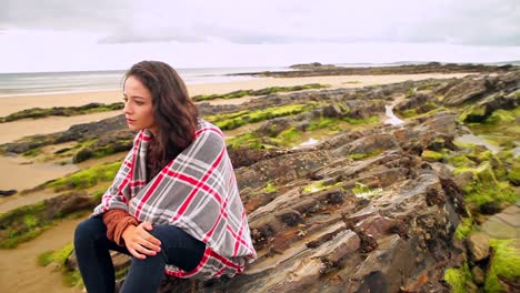 Pretty-brunette-wrapped-in-a-blanket-sitting-by-the-beach