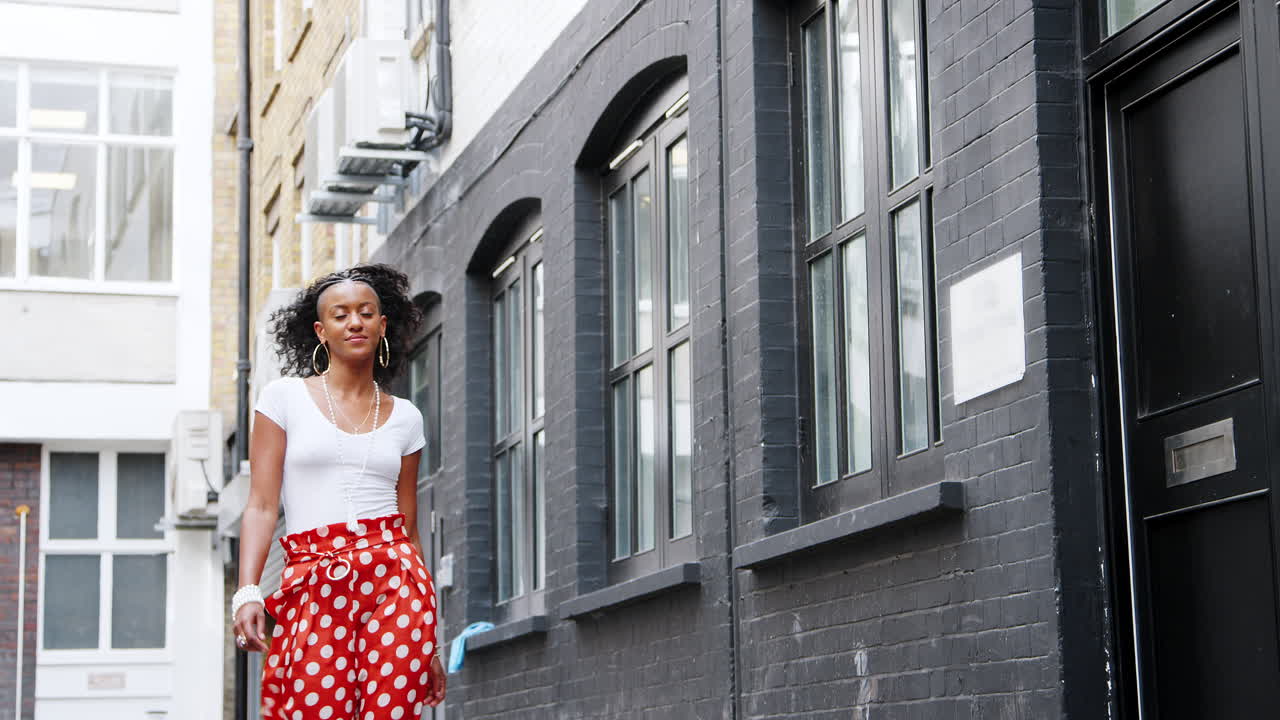 Fashionable young black woman wearing red polka dot trousers walking along a street, low angle
