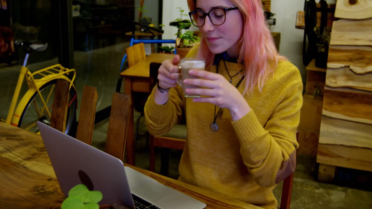 Giovane donna che sorseggia un caffè mentre usa un laptop al bar 4k