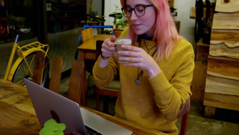 mujer joven tomando café mientras usa una computadora portátil en el café 4k