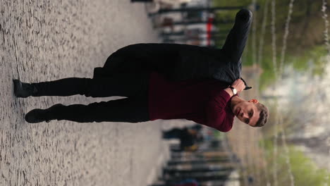 Vertical-Shot-of-Young-Handsome-Man-Walking-Outside-Alone-and-Puts-On-His-Jacket,-Cinematic-Street-Style