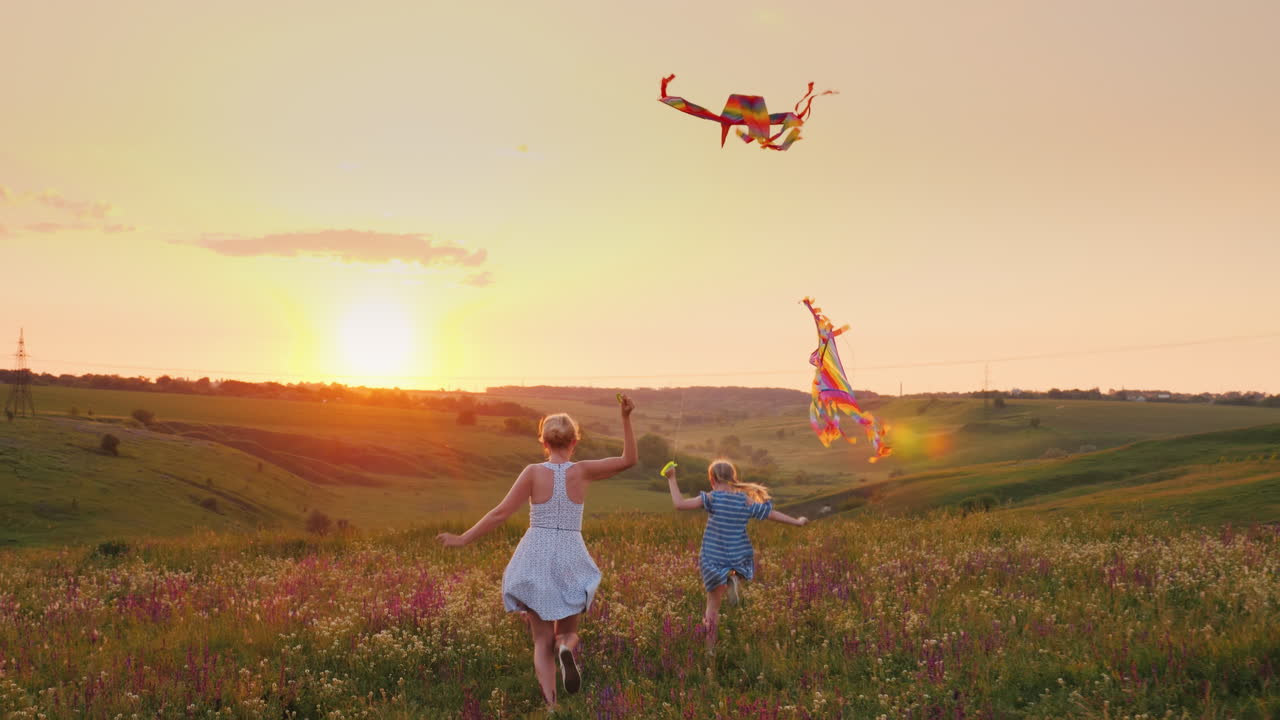 mamá con una hija pequeña corre hacia la puesta de sol con cometas