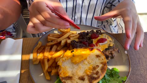 poniendo ketchup en una sabrosa carne de res de una hamburguesa con queso con papas fritas en un restaurante, tiro de 4k