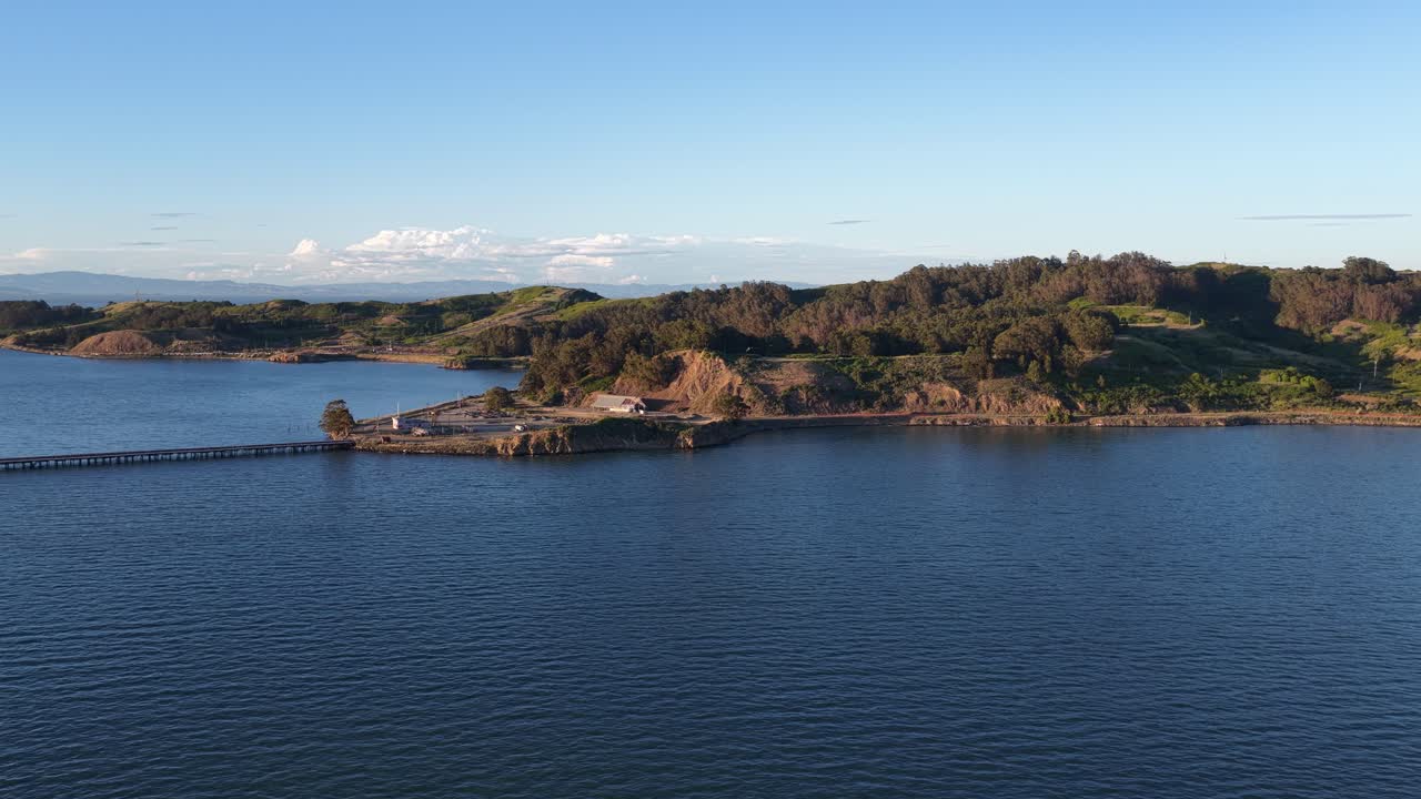 Perspectiva aérea com panorâmica lenta para a direita, mostrando as rochas de castro e o histórico Parque Praia Point Molate sobre a Baía de São Francisco, com as colinas douradas de Point San Pablo ao pôr do sol
