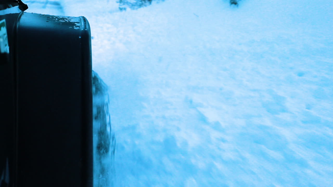 Off road tires of jeep kick up snow at the camera banked on the side of the icy road in the mountains
