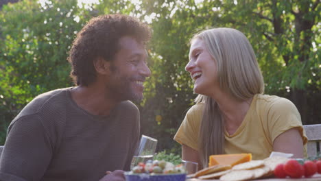 Amorosa-Pareja-Madura-Celebrando-Con-Champán-Mientras-Se-Sientan-A-La-Mesa-En-El-Jardín-Con-Bocadillos