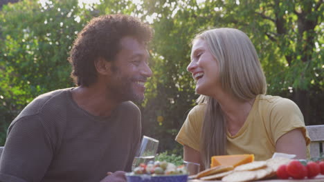 amorosa pareja madura celebrando con champán mientras se sientan a la mesa en el jardín con bocadillos