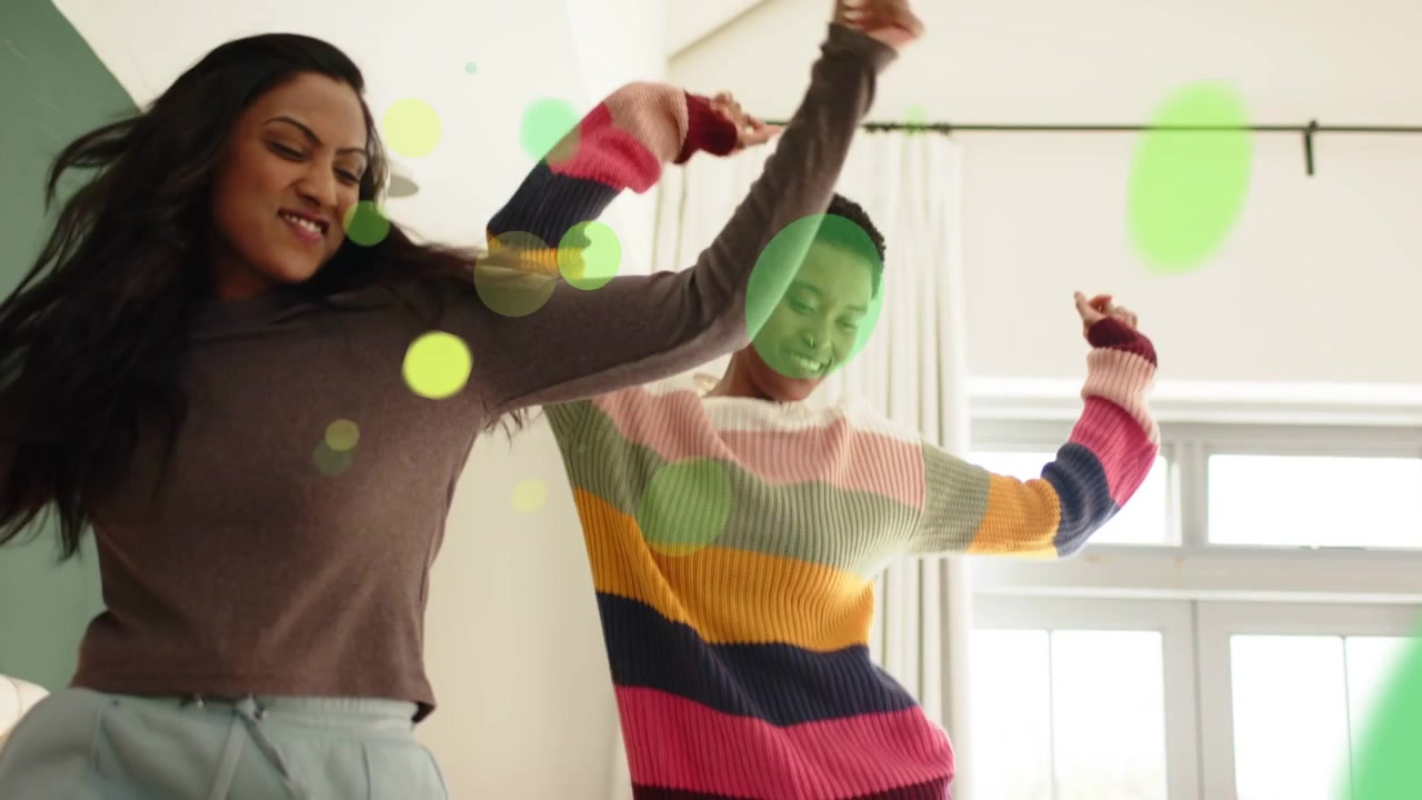 Two women stepping onto sofa sparking green circles drifting across frame, mirroring playful moves