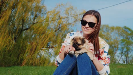 descansar en el parque con un perro y un bocadillo en el camino perrito caliente. una mujer joven se sienta en el lago en un parque jugando con su pug