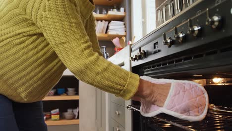 Old-lady-wearing-oven-gloves-taking-out-freshly-baked-muffins-from-oven-4K-4k