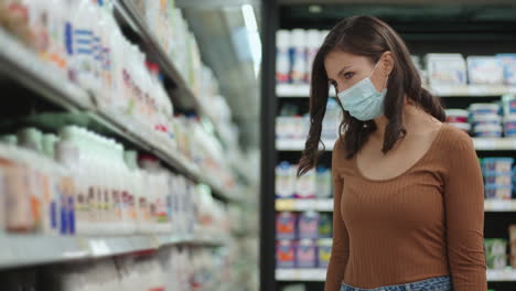 a girl goes to the refrigerator in a supermarket in a protective mask. buy products in a mask