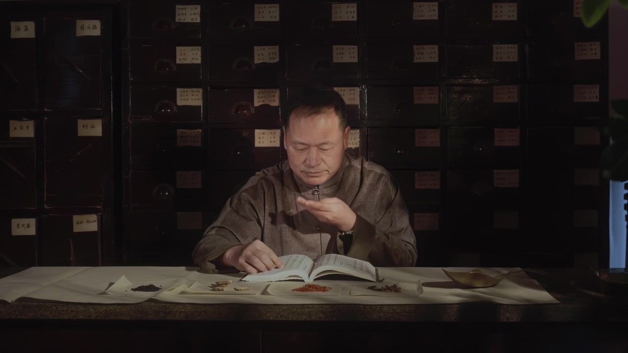 Traditional oriental herbalist medicine doctor researching each type of medicinal herb in ancient book, surrounded by precious medicinal herbs with ingredients prescription at clinic hospital